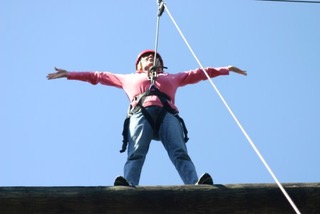 Jessica Shields Flowers, arms outstretched, walking a beam high above the trees on a ropes course, 2017